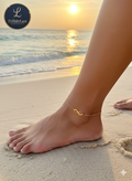 Gold anklet on a foot with a sunset over the ocean in the background